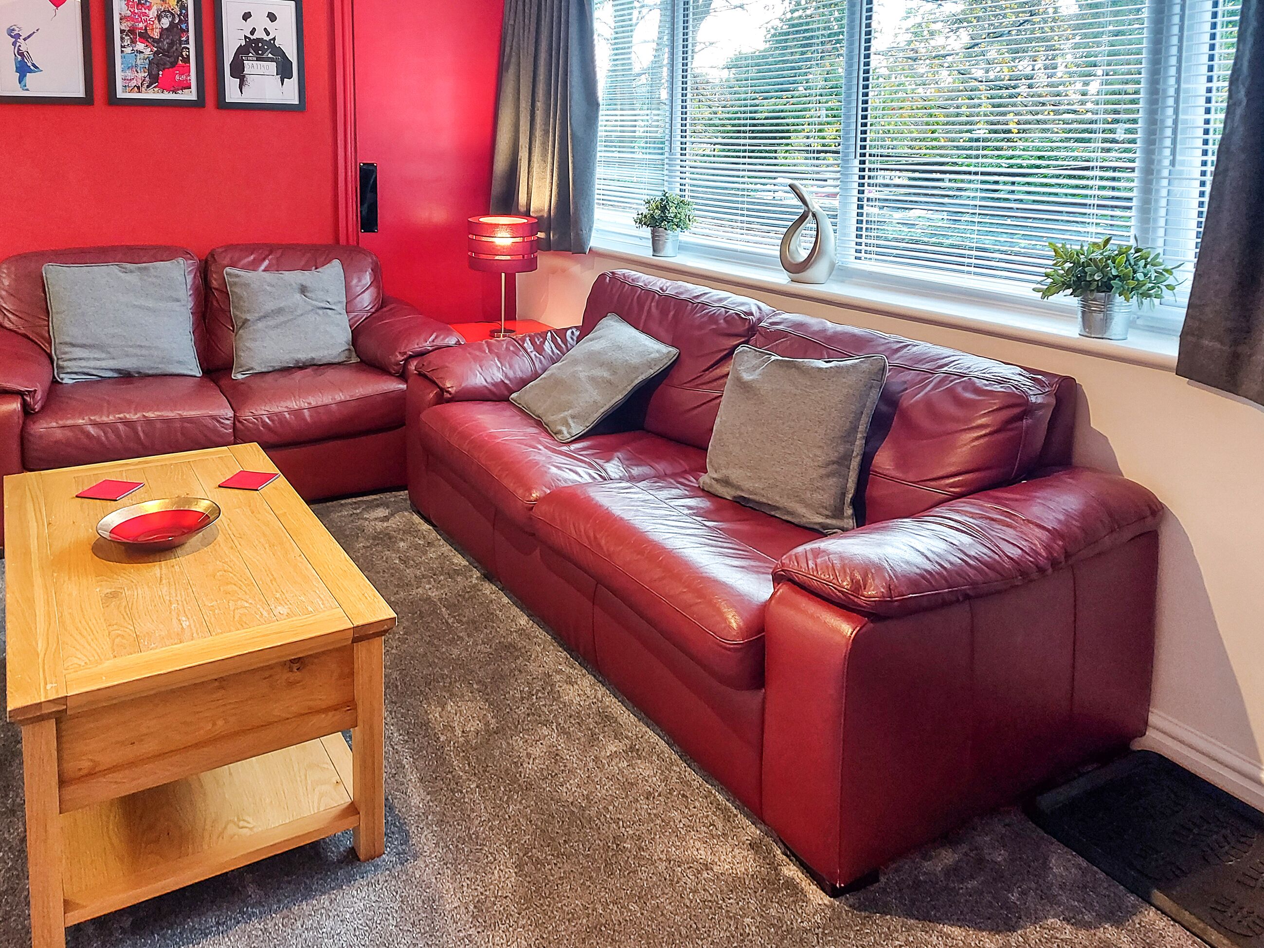 A living room with a red leather sofa, a wooden coffee table, and a red vase.