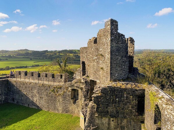 A historic stone castle ruin with a grassy foreground and a scenic countryside backdrop.
