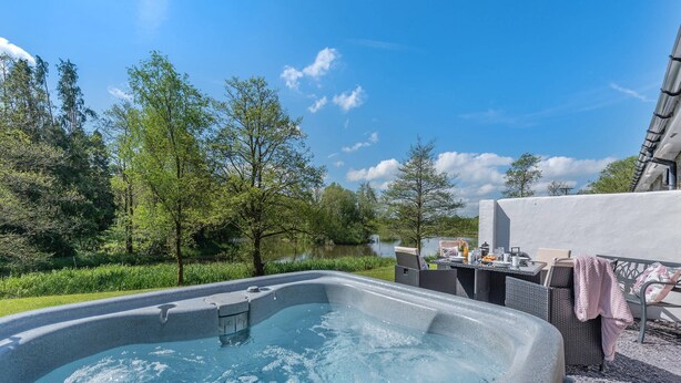 Un jacuzzi con una mesa y sillas, rodeado de follaje y árboles, con un cielo despejado al fondo.