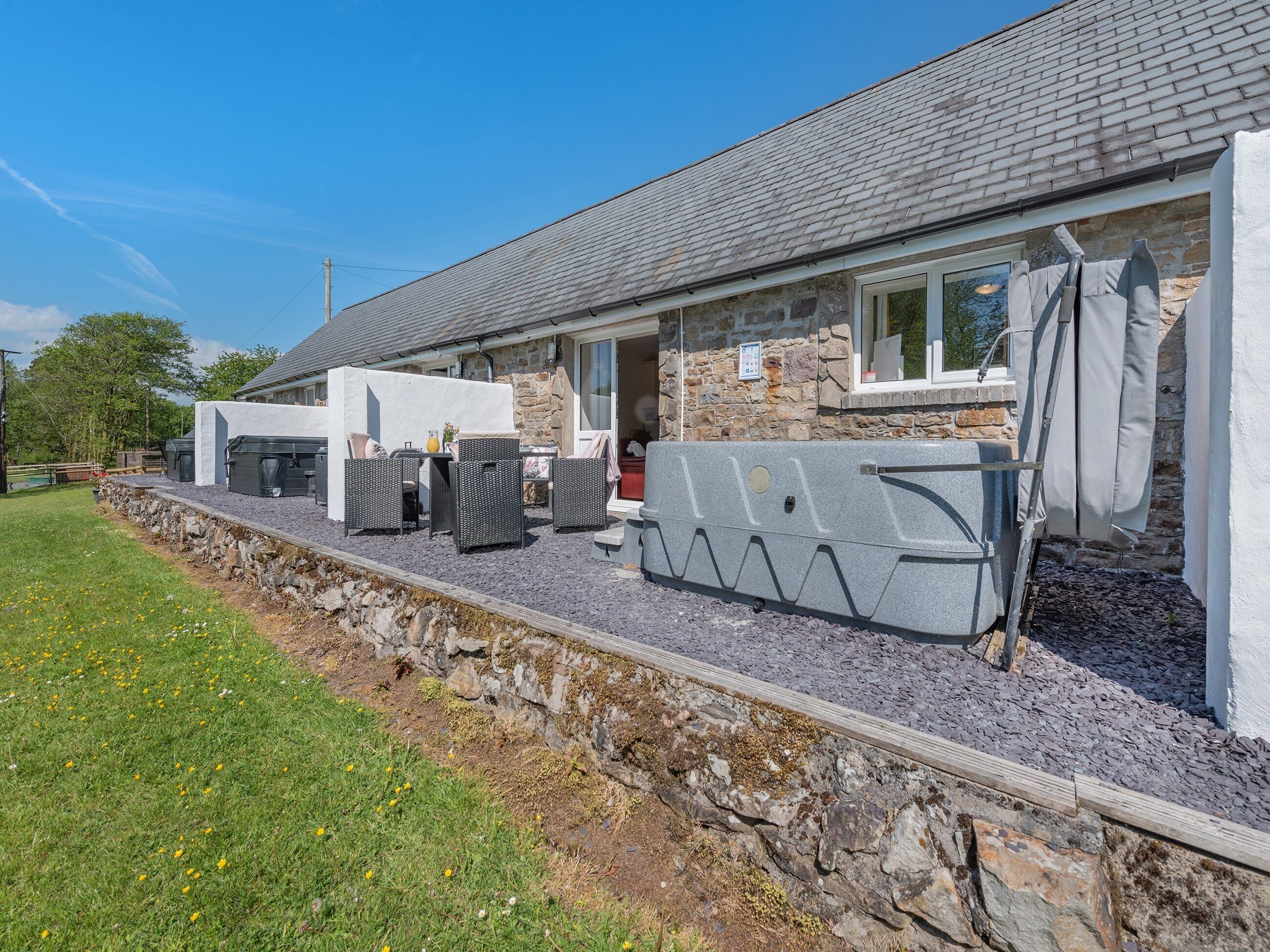 Ein Steinhaus mit Ziegeldach, Sitzbereich im Freien mit Korbmöbeln und einer überdachten Terrasse.