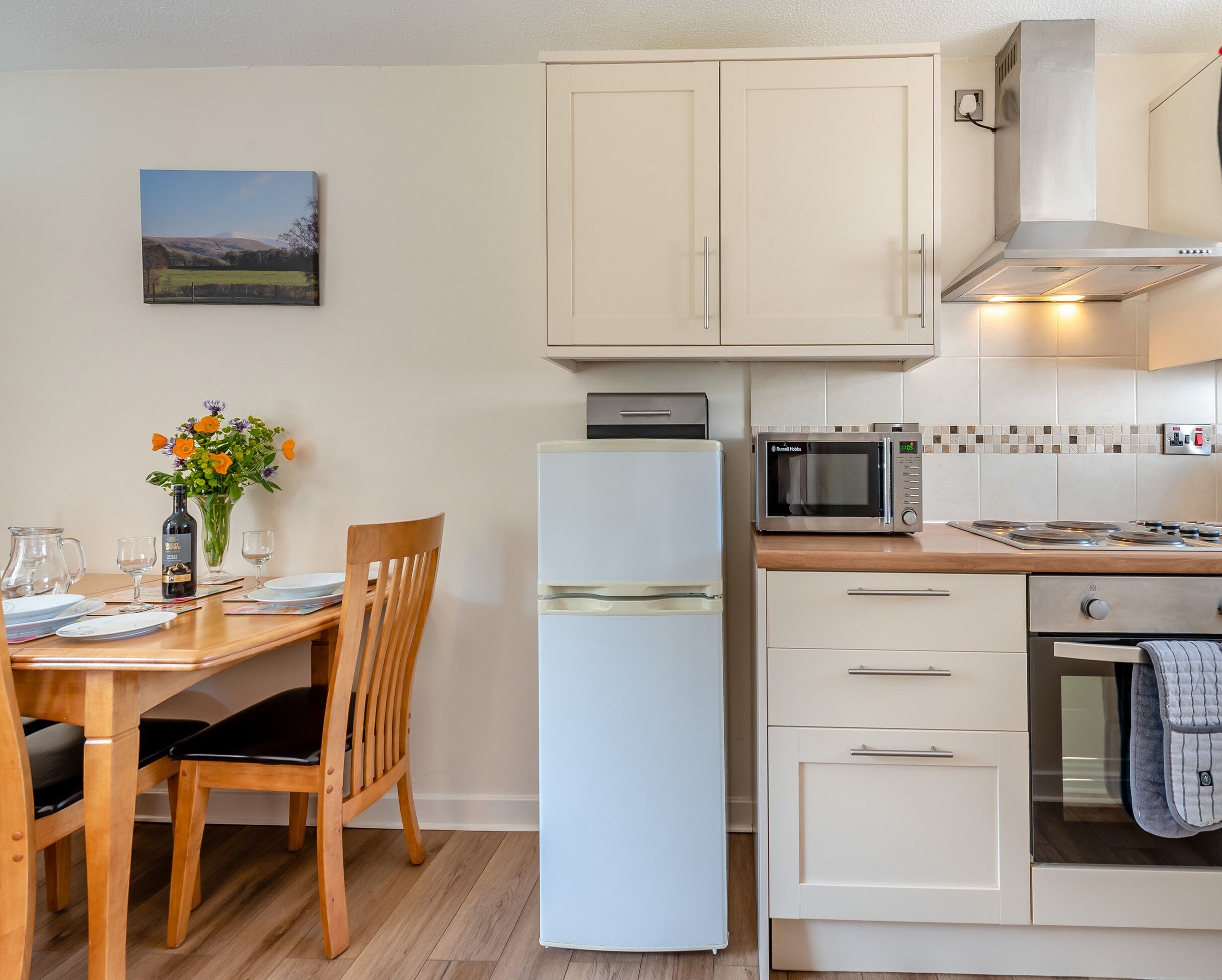 Una cocina compacta equipada con refrigerador, microondas y horno, junto a un comedor con mesa y sillas de madera.