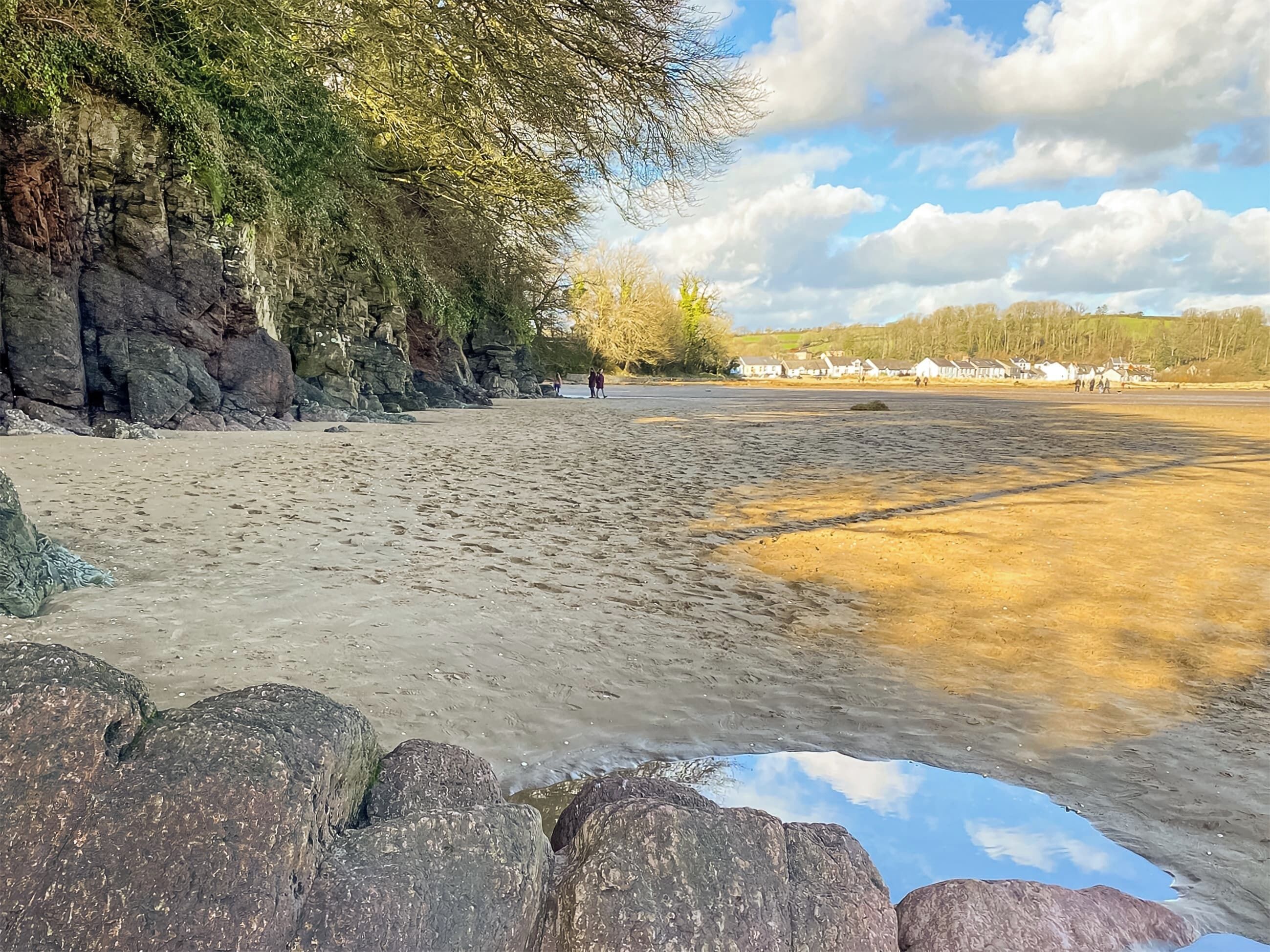 Une plage de sable avec des affleurements rocheux et un ciel dégagé.