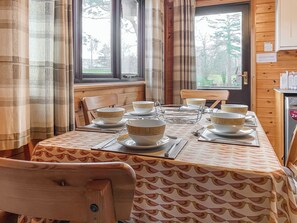 A dining table set with bowls and plates, wooden chairs, and a window with curtains. - 3 bedroom accommodation in Keswick (Keswick)
