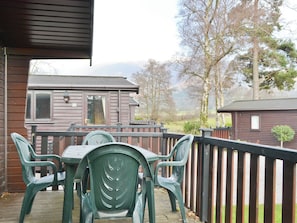 A wooden cabin with a balcony, green plastic chairs, and a view of trees and mountains. - 3 bedroom accommodation in Keswick (Keswick)
