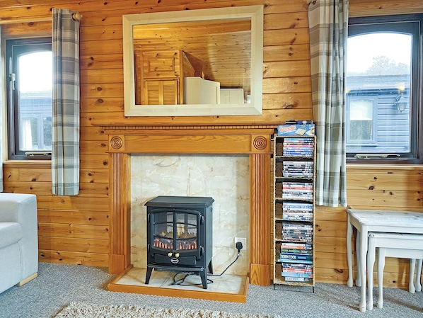 Una habitación acogedora con chimenea, paredes de madera, una estantería y un ventanal.