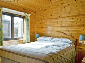 Una habitación con paneles de madera, una cama, dos lámparas de noche y un ventanal con cortinas.