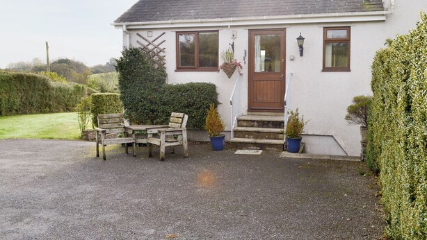 A white house with a brown door and windows, a wooden bench, and potted plants. - 1 bedroom accommodation in Dartington, Totnes (Dartington, Totnes)