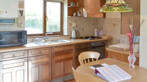 A kitchen with wooden cabinets, a microwave, a sink, a stove, and a dining table with a vase. - 1 bedroom accommodation in Dartington, Totnes (Dartington, Totnes)
