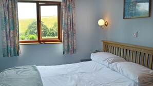 A bedroom with a large bed, a window with curtains, a nightstand, and a wall-mounted light fixture. - 1 bedroom accommodation in Dartington, Totnes (Dartington, Totnes)