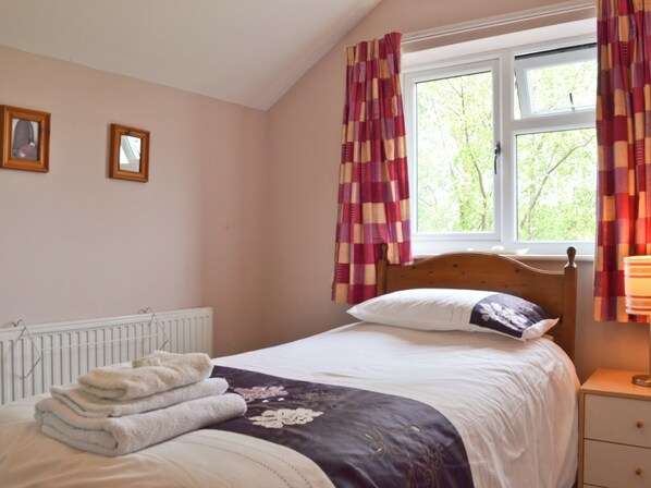 A bedroom with a bed, a radiator, a window with curtains, and a bedside table with a lamp.
