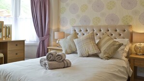A neatly made bed with rolled towels, a tufted headboard, and a patterned wallpaper. - Cliff Railway Apartment (Aberystwyth)