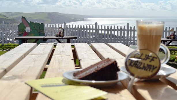 A picnic table with a slice of cake, a glass of coffee, and a sign reading "CLIFF HARVARD". - Cliff Railway Apartment (Aberystwyth)