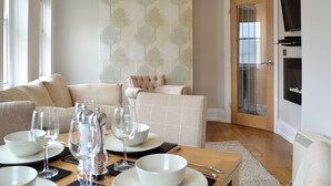 A dining area with a table set for four, a sofa, a chair, and a television mounted on the wall. - Cliff Railway Apartment (Aberystwyth)
