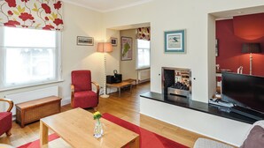 A living room with a fireplace, a television, a red chair, and a wooden coffee table. - 3 bedroom accommodation in Yarmouth (Yarmouth)