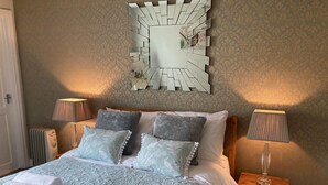 A neatly made bed with patterned bedding, two bedside lamps, a decorative mirror, and a radiator. - All on the Ground Floor: 
Open plan living space. (Lockton, near Pickering)