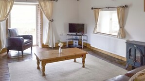 A cozy living room with a wooden table, a comfortable chair, a television, and a fireplace.