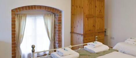 A bedroom with two beds, a wooden wardrobe, a brick archway, and a window with curtains.