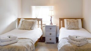 A bedroom with two single beds, a nightstand with a lamp, and a window with curtains.