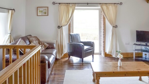 A cozy living room with a wooden staircase, a leather sofa, a black armchair, and a wooden coffee table.