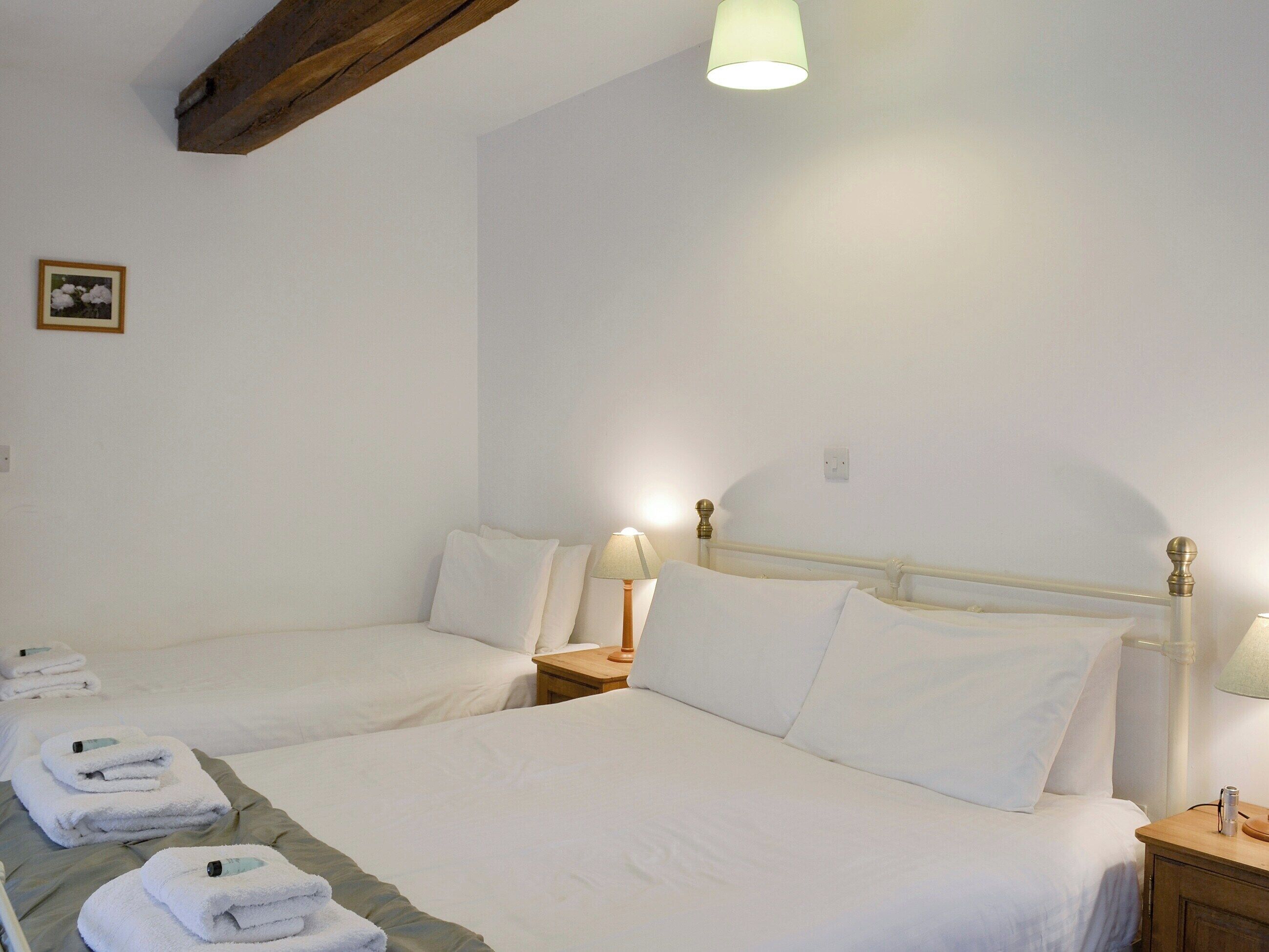 A hotel room with two beds, a wooden ceiling beam, a framed picture on the wall, and a bedside lamp.
