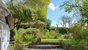 Ein Garten mit Steintreppen, die zu einem weißen Gebäude mit Strohdach führen.