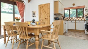 Ein Holzespeisetisch mit Stühlen, eine Küche mit kariertem Fliesenspiegel und ein Fenster mit Blick auf Grünflächen.