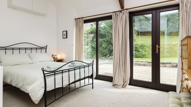 Ein Schlafzimmer mit einem Bett, einem Nachttisch, einem Holzschrank und einer großen Glasschiebetür, die zu einem Garten führt.