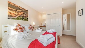A hotel room with a large bed, a red blanket, white pillows, a painting of a landscape, a desk with a lamp, and a white door. - Buzzard Cottage - 27940 (Stirling)