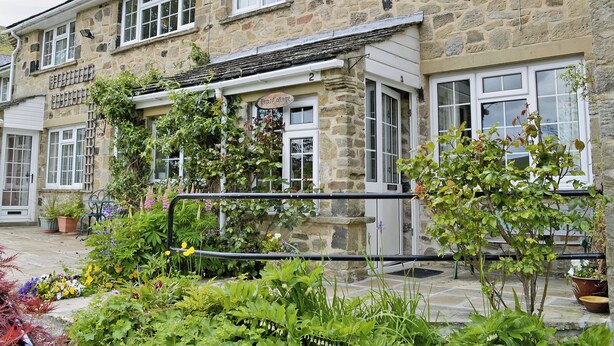 A stone building with multiple windows and a sign reading 'Bristol Cottage.' - 20 steps to entrance with handrail. (Burnsall near Grassington)