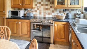 A kitchen with wooden cabinets, a stainless steel stove, a microwave, and a tiled backsplash. - 20 steps to entrance with handrail. (Burnsall near Grassington)