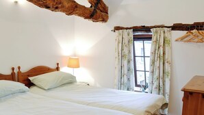 Un dormitorio con dos camas, cabeceros de madera, una lámpara, cortinas florales y una ventana con vistas.