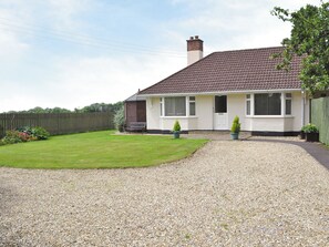 Une maison de plain-pied avec une allée en gravier, une pelouse devant et une clôture en bois.