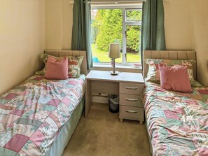 Une chambre avec deux lits simples, un bureau et une fenêtre avec des rideaux.