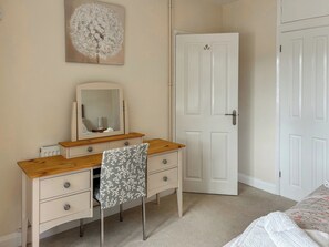 Une chambre à coucher avec une commode en bois, un miroir, une chaise, un lit et une porte blanche.