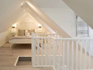 A bedroom with a sloped ceiling, a bed with white bedding, two bedside lamps, and a white railing. - 3 bedroom accommodation in Helstone, near Camelford (Helstone, near Camelford)
