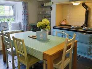 A kitchen with a dining table, chairs, a vase with flowers, and a refrigerator.