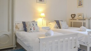 A double bed with white bedding and nautical-themed pillows, a bedside table with a lamp, and a small cabinet with decorative items. - 3 bedroom accommodation in Helstone, near Camelford (Helstone, near Camelford)