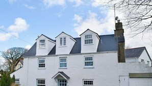 A two-story house with a white exterior, multiple windows, a chimney, and a small patio area with a table and chairs. - 3 bedroom accommodation in Helstone, near Camelford (Helstone, near Camelford)