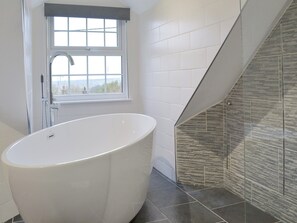 A modern bathroom with a freestanding bathtub, a window with a view, and a glass shower enclosure.