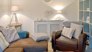 A living room with a sofa, armchair, side table, lamp, wall clock, and a bookshelf. - 3 bedroom accommodation in Helstone, near Camelford (Helstone, near Camelford)