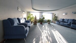 Un vaste espace d’attente avec des canapés bleus disposés en rangées, un petit sapin de Noël et des plantes en pot.