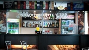 Un espace bar avec des étagères remplies de bouteilles d’alcool, un présentoir réfrigéré et un coin salon avec des chaises.