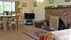 A cozy living room with a fireplace, a dining area with a table and chairs, and a television. - 2 bedroom accommodation in Aughton, near Marlborough (Aughton, near Marlborough)