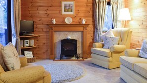 Interior acogedor de una cabaña de troncos con chimenea, dos sillones, un televisor y una estantería.