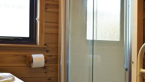 Un interior de madera con puerta de ducha de vidrio, un dispensador de papel higiénico y una ventana.
