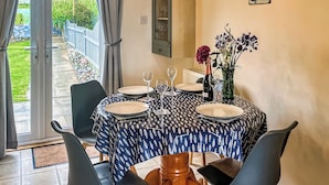 Un coin repas avec une table dressée pour deux personnes, agrémenté d’une nappe à motifs, de deux chaises, d’un vase avec des fleurs et d’une bouteille de vin.