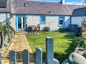 Une maison avec un chemin pavé menant à une table et à des chaises en bois situées à l’extérieur.