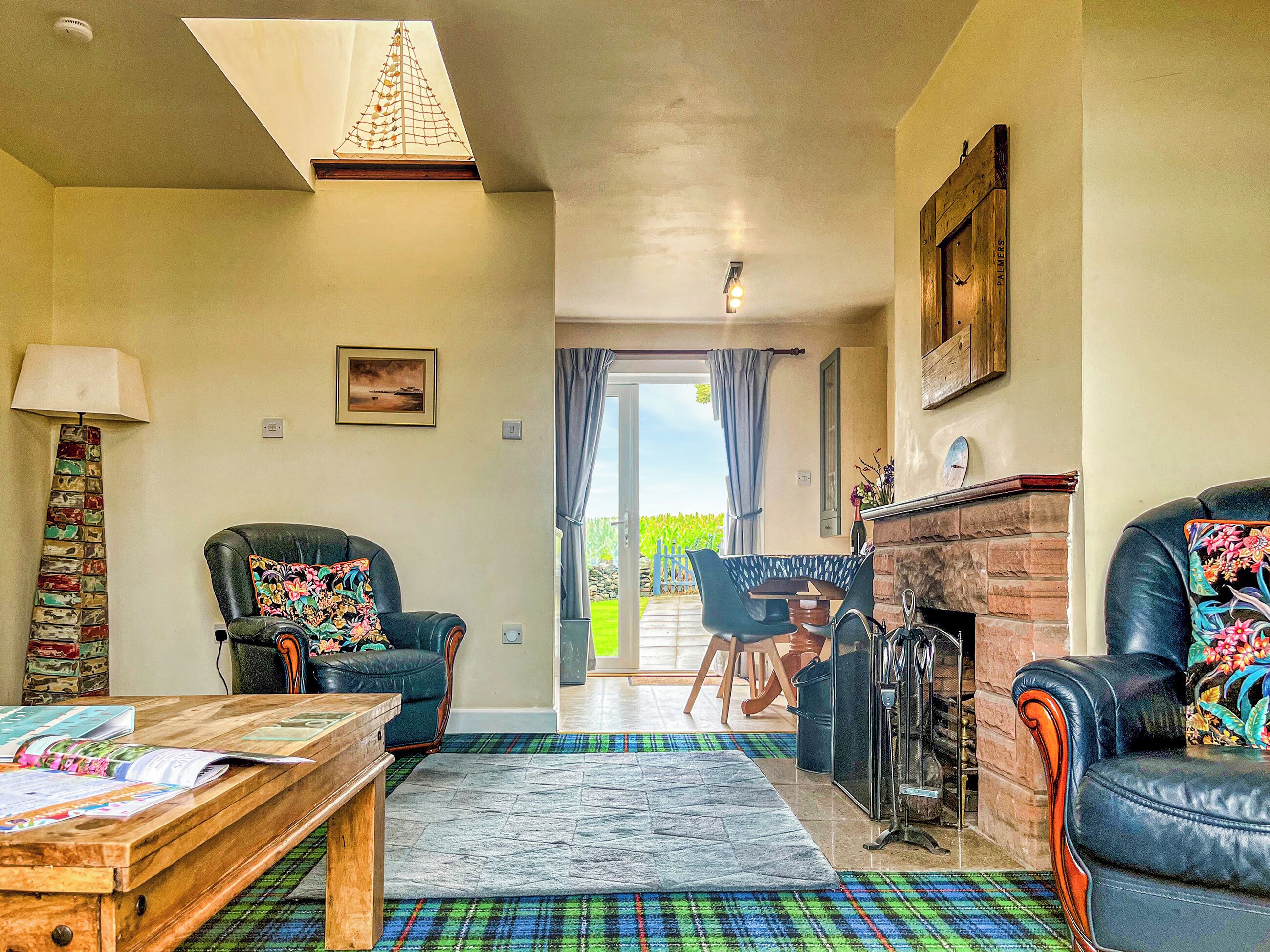 A living room with a fireplace, two leather armchairs, a coffee table, and a view through a glass door to the outside.