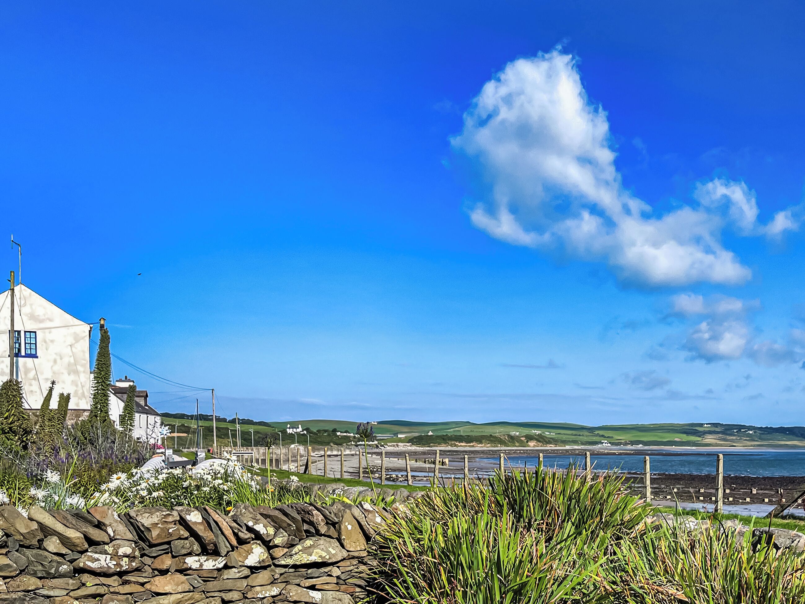 A coastal landscape with a stone wall, a white building, and a view of the sea.