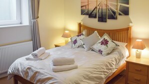 Una cama bien hecha con sábanas blancas y almohadas florales, un cabecero de madera y vistas a un muelle a través de una ventana.